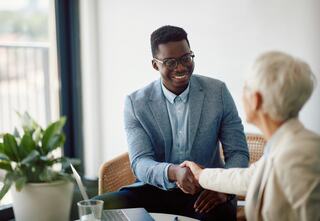 two professionals shaking hands while seated at a small office side table