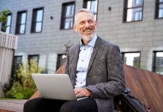 cheerful man with a laptop sitting on a bench outside